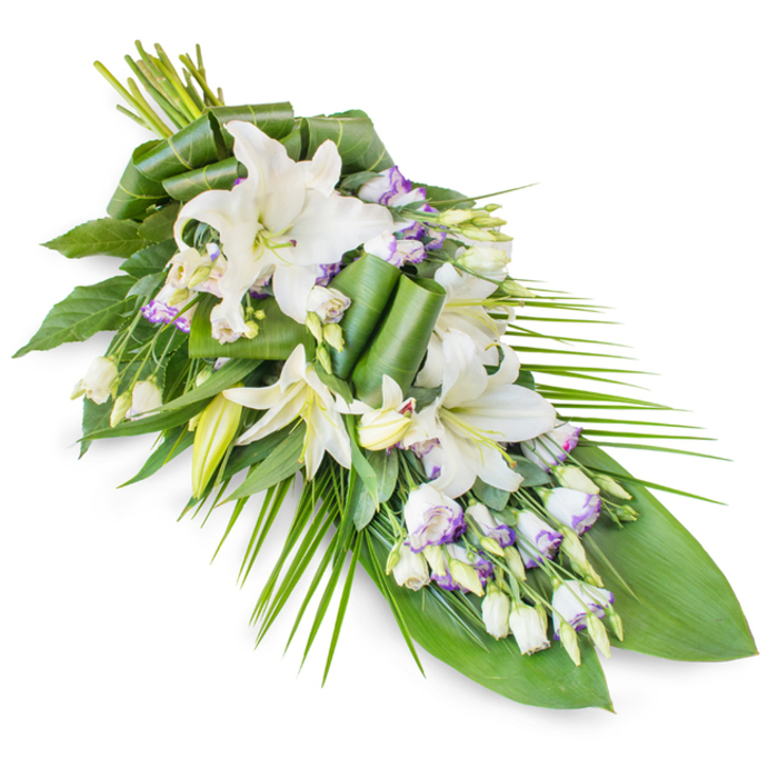 A large, teardrop-shaped funeral spray of white lilies and lisianthus is captured against a seamless white background, its diagonal orientation adding a sense of movement and thoughtful design. At the upper section, several prominent oriental lilies in pure white are clustered together, some fully open to reveal their gently arching petals and soft yellow-green stamens, others still enclosed in elegant buds that hint at unfolding stories and cherished memories. Interspersed among these grand blooms are stems of lisianthus, their more delicate white flowers edged with thin rims of lavender or pale purple, lending a soft touch of colour and a feeling akin to twilight settling over the quieter corners of South Hornchurch. Numerous unopened lisianthus buds punctuate the line of the spray, giving extra texture and suggesting continuity and hope. Surrounding the flowers is an abundant layer of greenery: wide, dark green leaves serve as a grounding base, while several leaves have been expertly rolled and sculpted into neat curls and folded accents, demonstrating the precision and care of South Hornchurch Florist. Long, slender palm-like fronds arc gracefully outward, particularly along the right-hand side and the tapering lower end, emphasising the arrangement's elongated silhouette and adding a sense of serene expansion. The interplay of crisp white blooms, gentle lavender edges, and deep, forest-green foliage conveys peace, reverence, and comforting support. This dignified tribute appears perfectly suited for display at a funeral service, memorial gathering, or graveside in South Hornchurch and nearby Rainham, offering a calm, elegant floral expression of condolence and enduring affection.